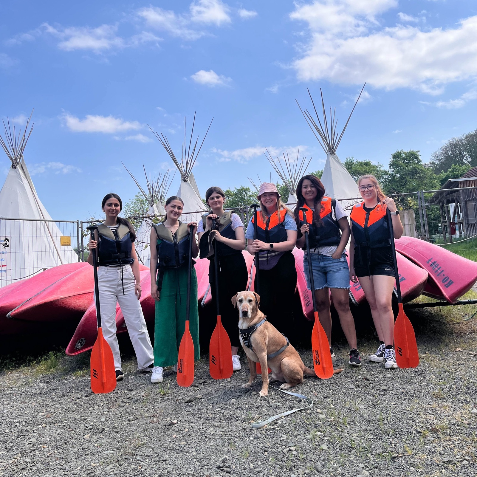 Gruppe in Schwimmwesten mit Paddeln und Hund vor Kanus an der Lahn